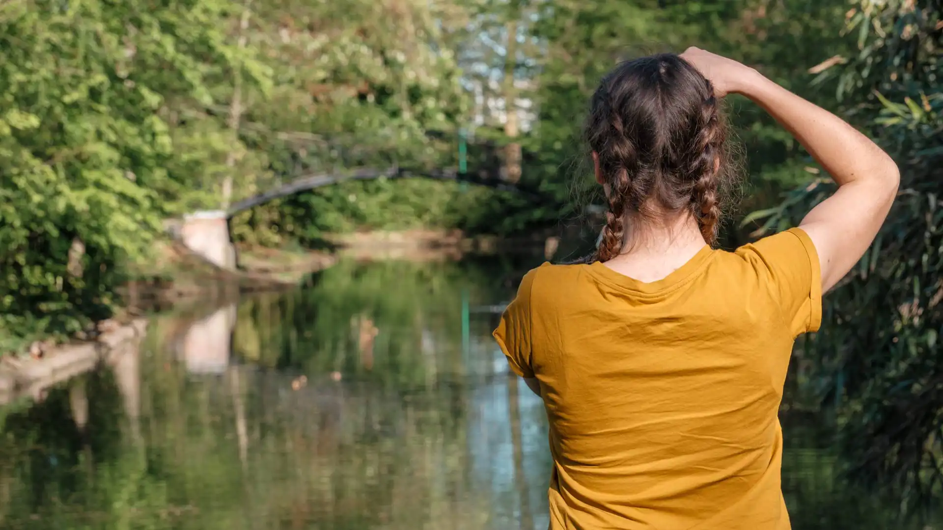Femme de dos avec des tresses et un tee-shirt jaune prenant une photo dans un parc à Malines