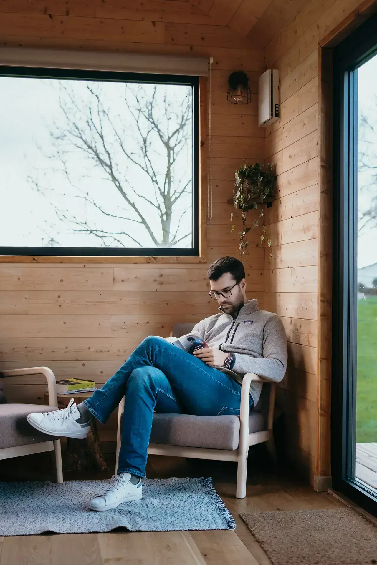 Homme lisant un livre sur un fauteuil simple dans une tiny house.