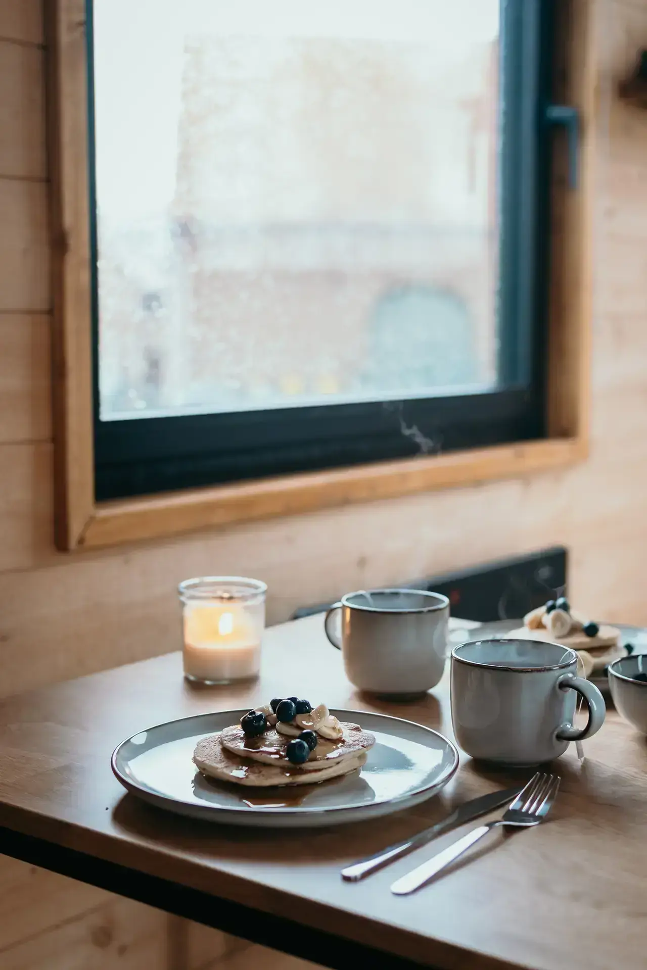 Assiette de pancakes à la myrthille avec une bougie et une tasse de thé fumante dans une Tiny House